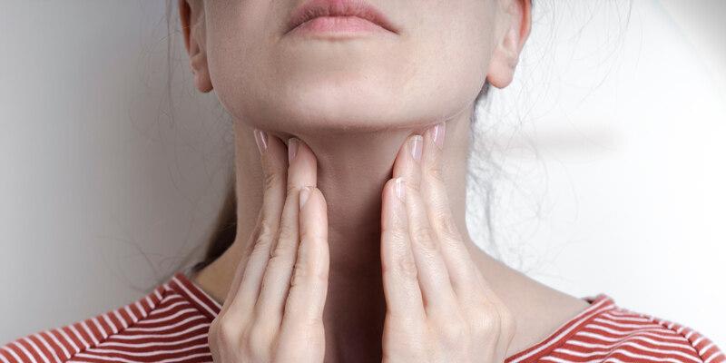 Hormony tarczycy - za co odpowiadają? Kobieta dotykająca szyi w miejscu, gdzie znajdują się gruczoły tarczycy.