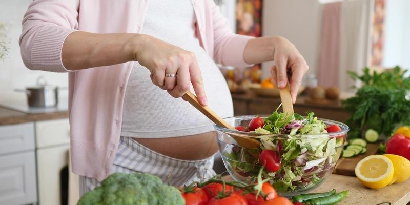 Dieta w ciąży - dobre produkty, propozycja jadłospisu. Kobieta w ciąży przygotowuje zdrową sałatkę.