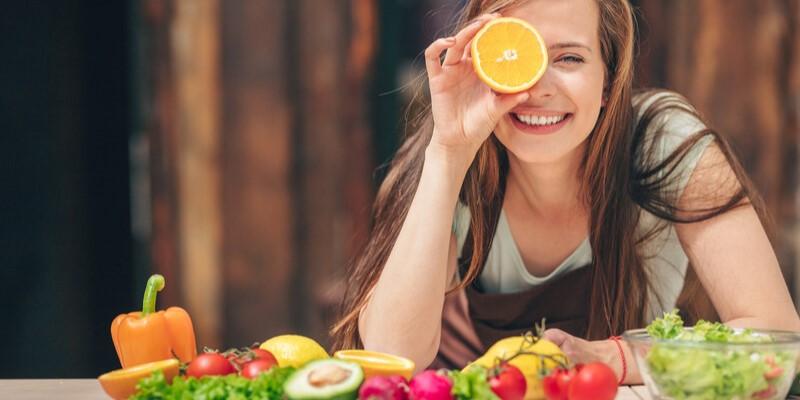Karotenoidy - zdjęcie przedstawia kobietę trzymającą pomarańczę w dłoni oraz warzywa na stole