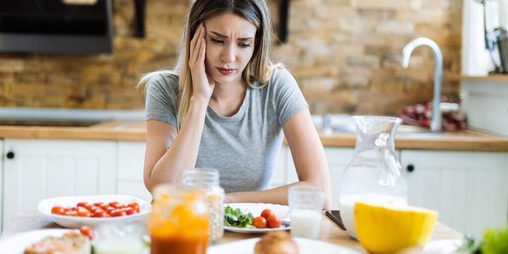 złe samopoczucie po jedzeniu - smutna kobieta siedząca przy stole z jedzeniem