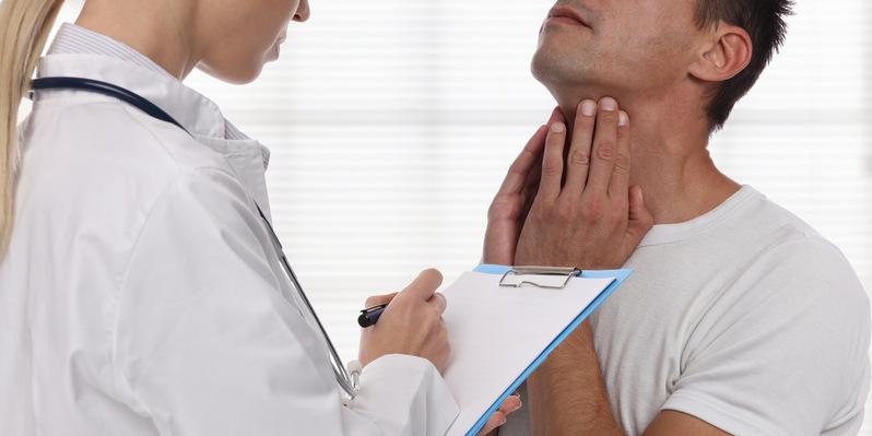 Chłoniak Hodgkina – objawy, rokowania, leczenie. Mężczyzna wskazuje na bolącą szyję podczas konsultacji lekarskiej.