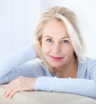 Active beautiful middle-aged woman smiling friendly and looking in camera in living room. Woman's face closeup. Realistic images without retouching with their own imperfections. Selective focus.